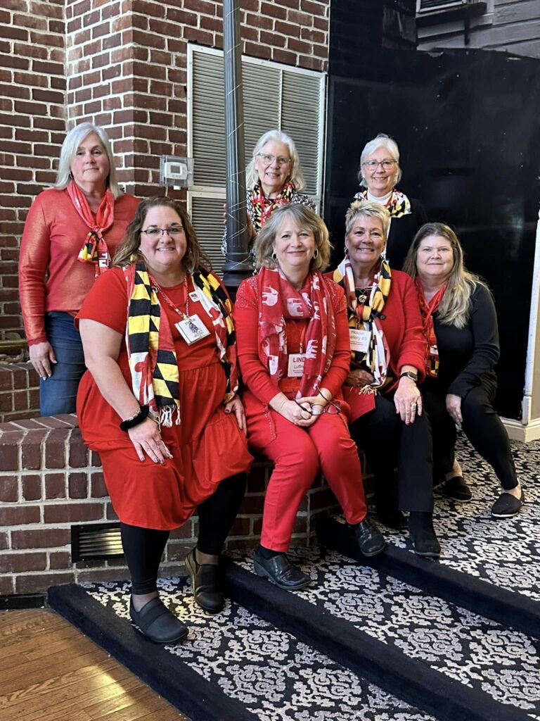 Seven WCRW members wearing red clothing and Maryland-themed scarves gathered together in front of a brick wall
